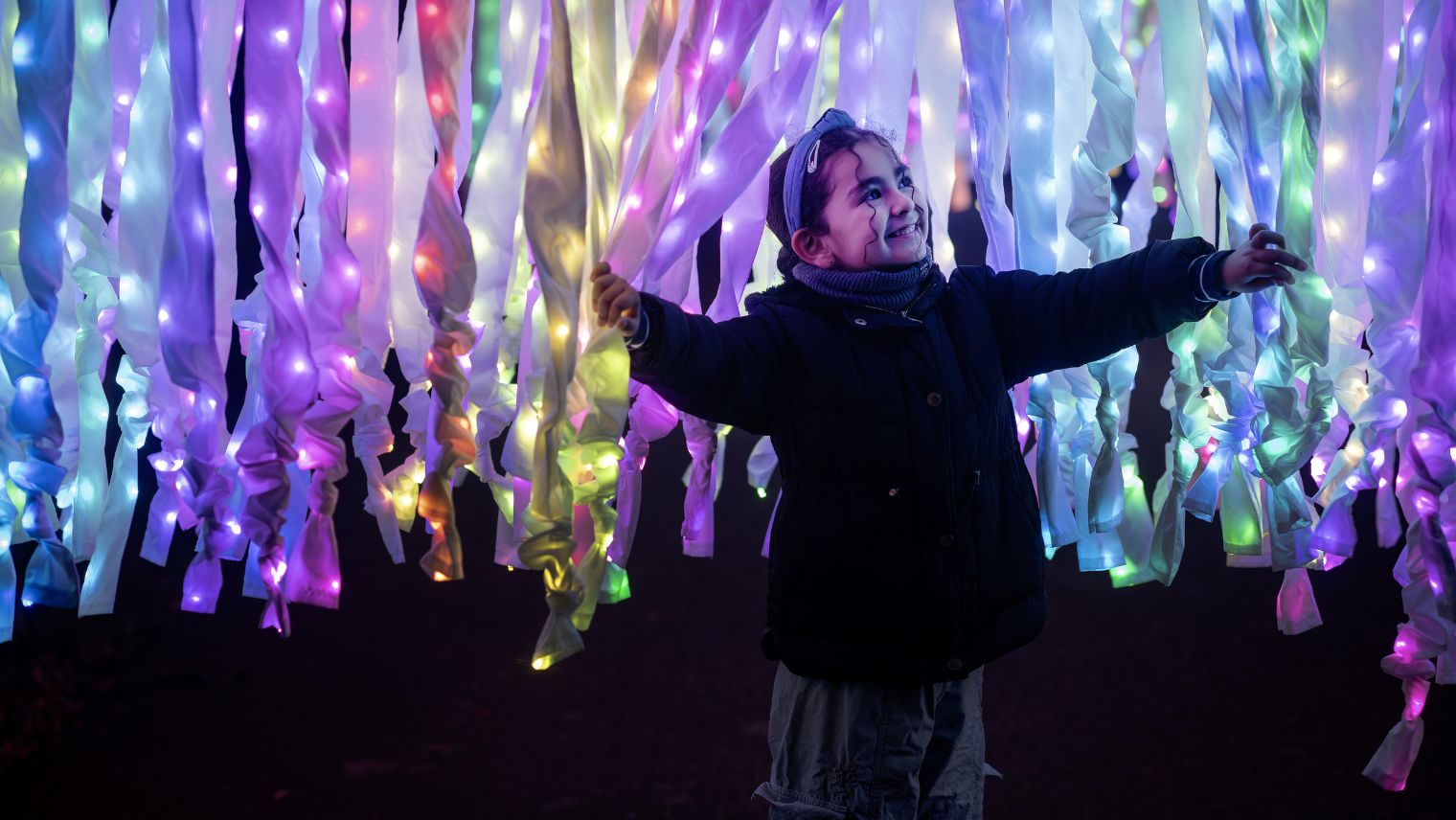 Young girl playing below light filled streamers from a tree