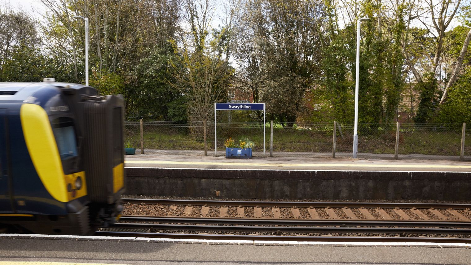 View of platform with sign saying Swaythling in centre of picture. Front of trains entering shot from left