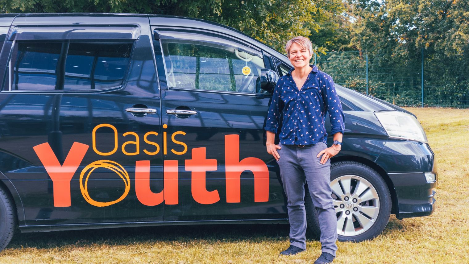 Person standing by the front wing of a blue van which says Oasis Youth on the side
