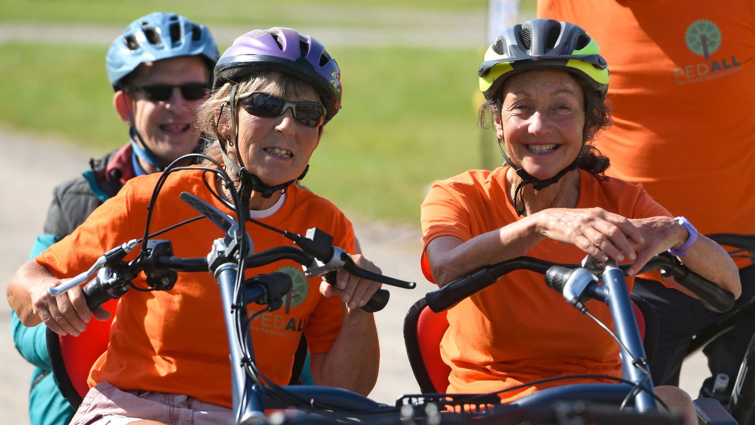 Two women in orange t-shirts and cycle helmets on a seated bicycle