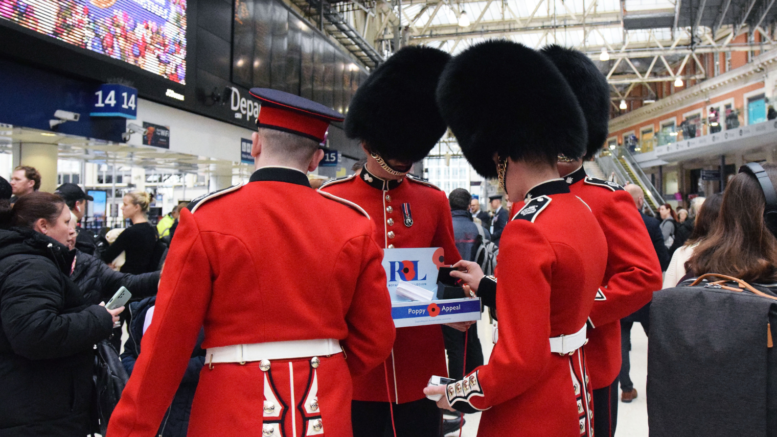 Four Guardsmen in red coats standing around a collecting tray at London Waterloo station