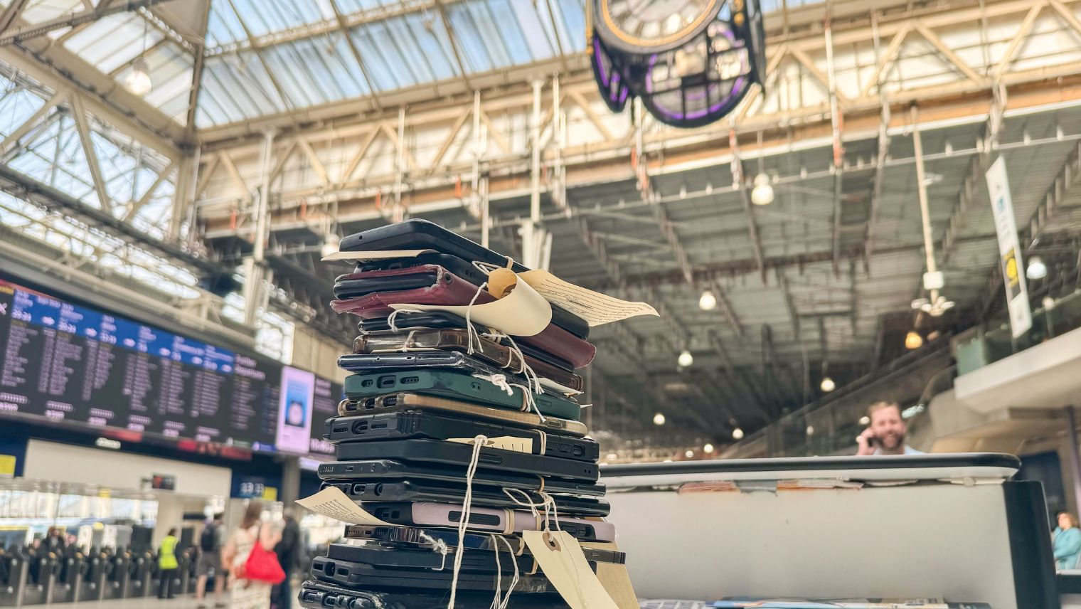 A pile of lost phones tied into a bundle with a label on the floor of Waterloo station under the clock