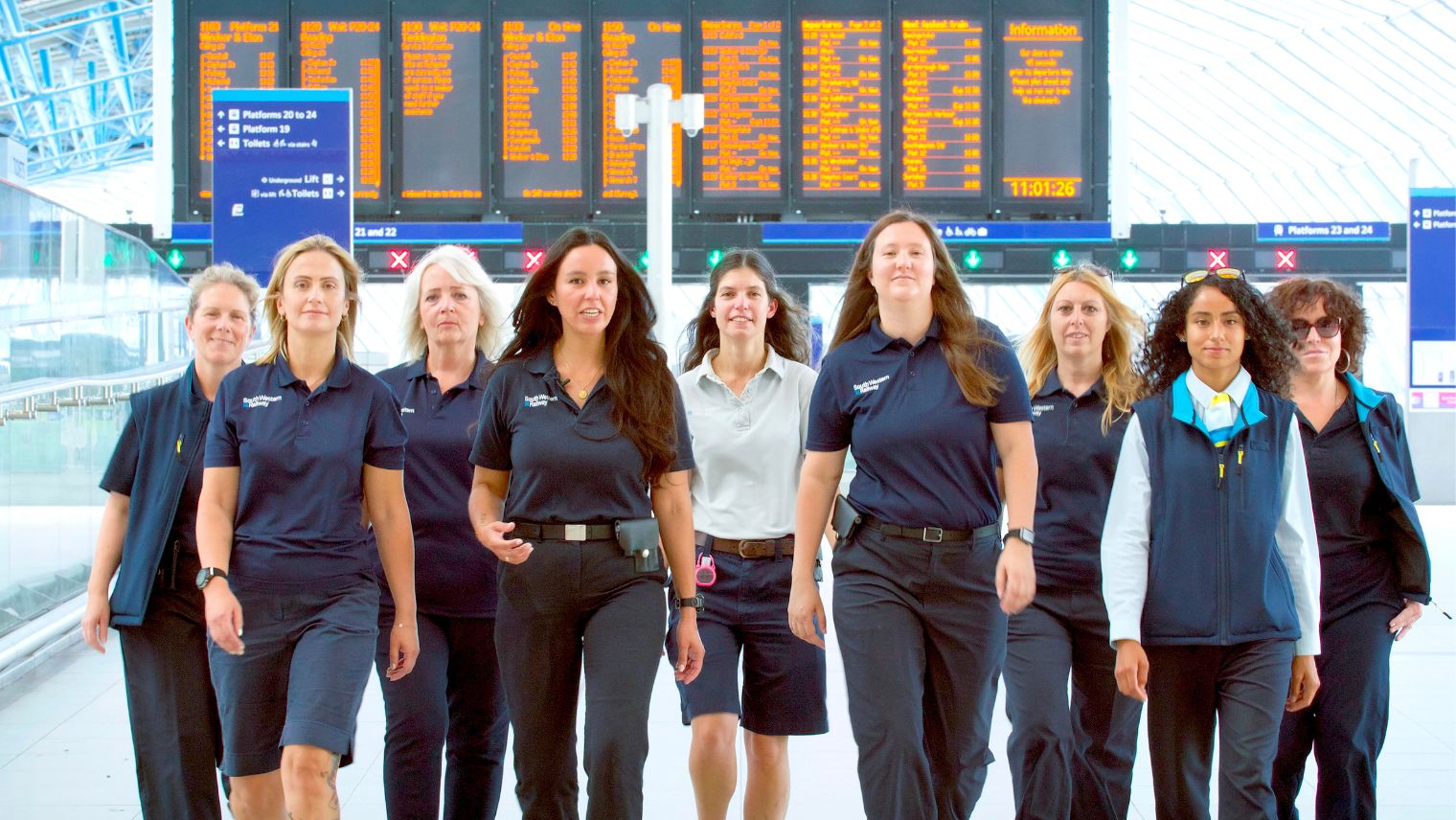 Group of nine women train drivers walking toward the camera with the Waterloo gateline behind them