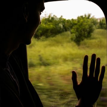 Photo of a silhouette of a person looking out of a train window into scenery