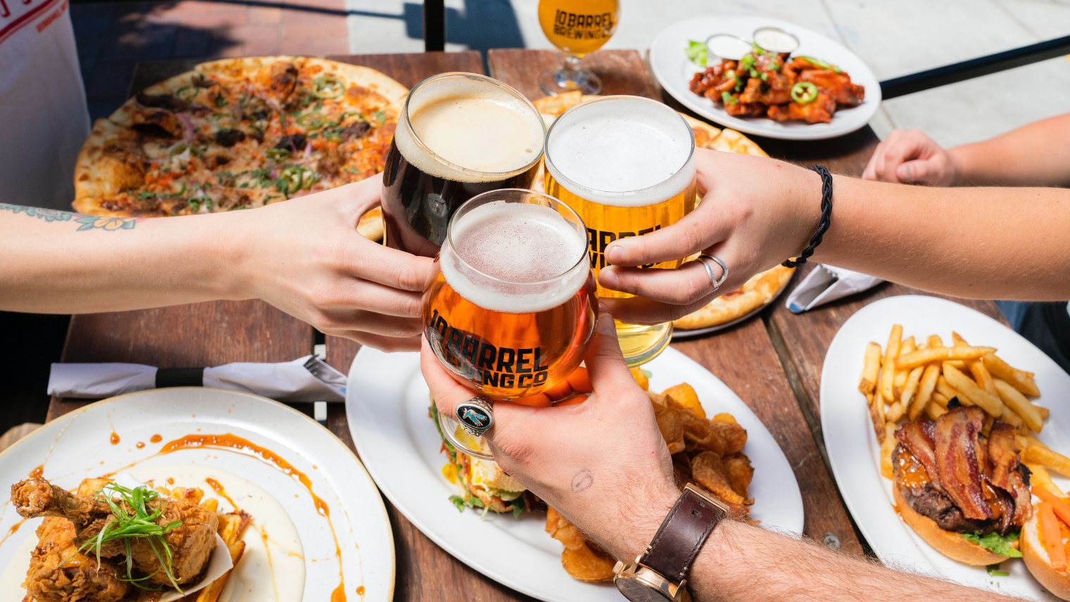 Image of 3 people holding beers, with plates of food around them at a table