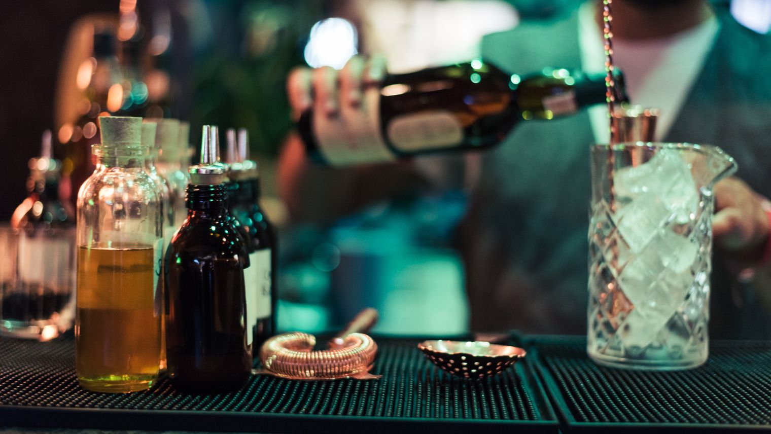 Faceless bar tender pours a dark liquor into a tall glass filled with ice