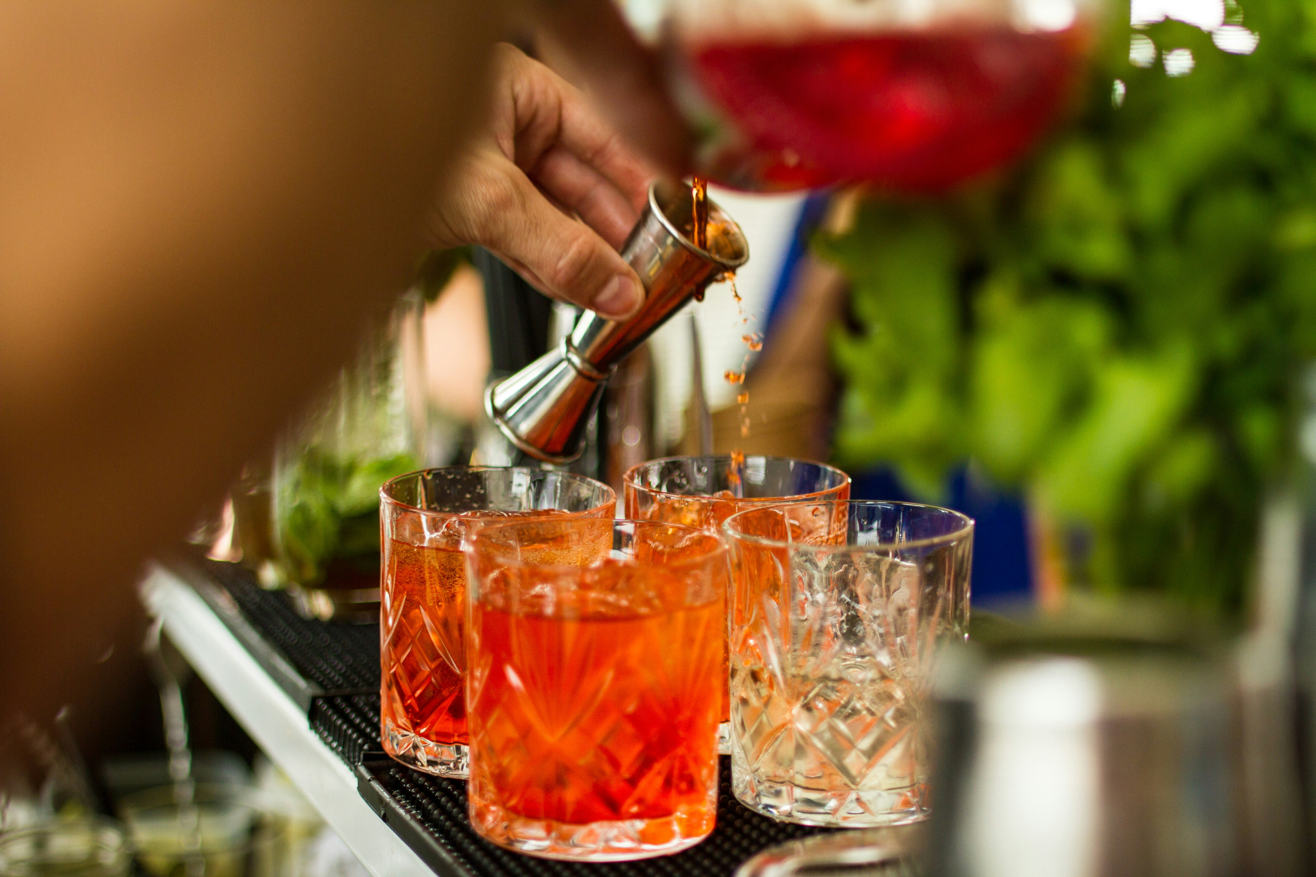 A barman serves up a cocktail from a shaker to a Martini glass over a crowded bar with people watching on