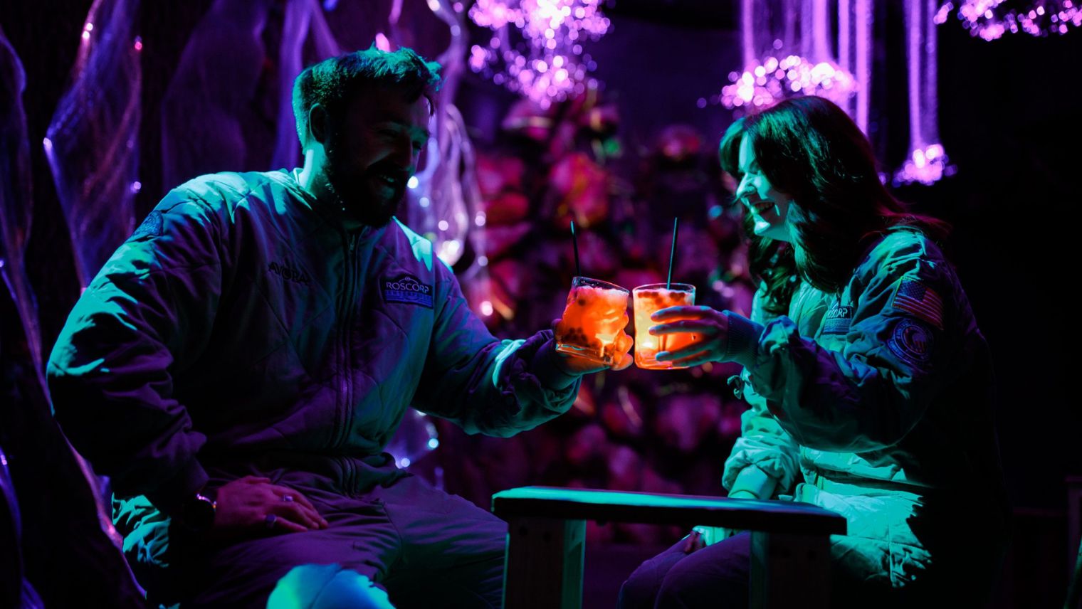 Two people enjoying cocktails in hazy, neon lit bar