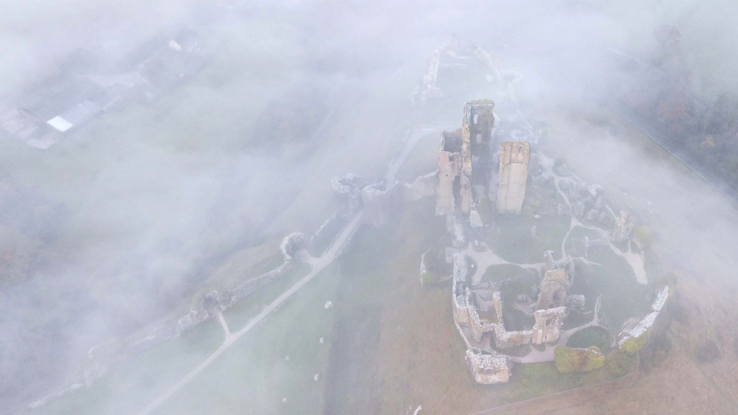 An overhead image or bird's eye view of the ruins of Corfe Castle surrounded by mist